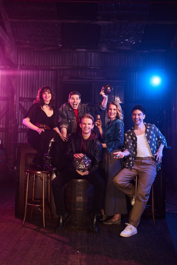Cast members of the Australian production of Dungeons & Dragons: The Twenty-Sided Tavern pose onstage. The ensemble exudes energy and playfulness, with colorful lighting evoking a classic tabletop RPG atmosphere.