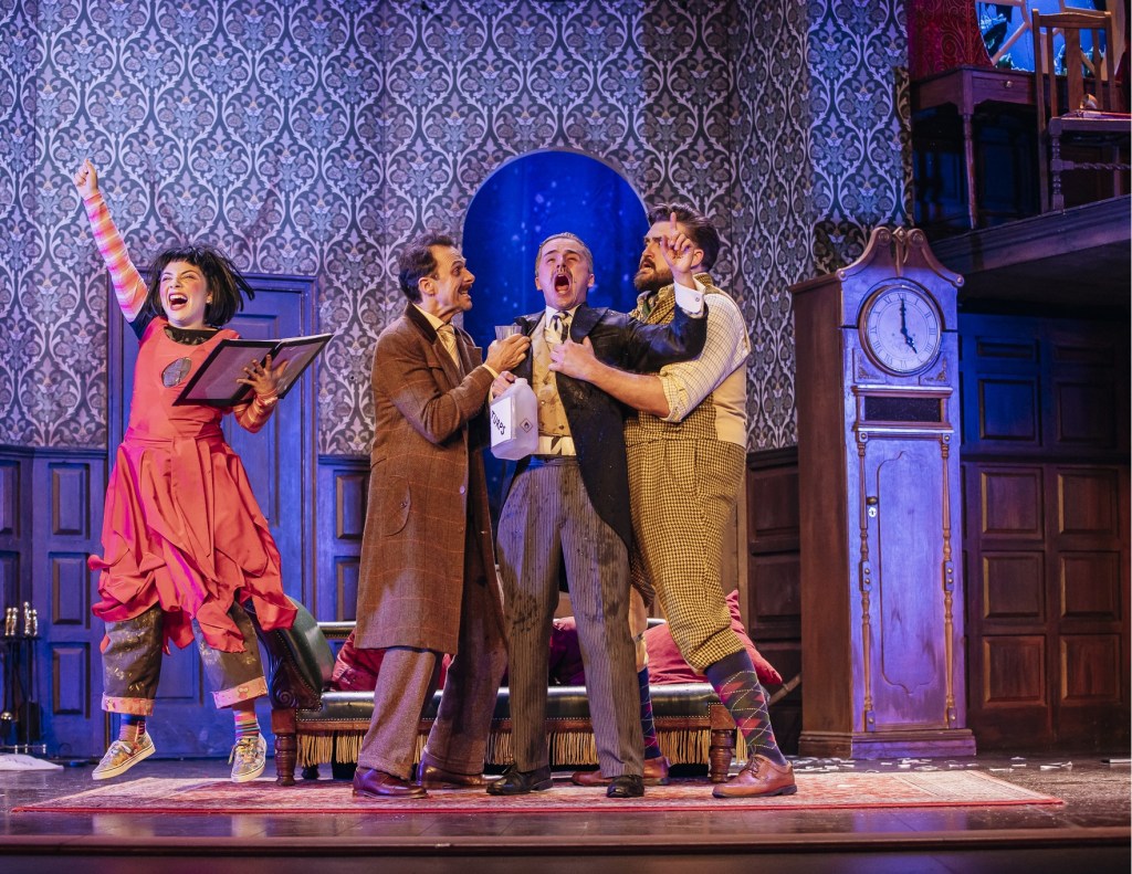 A scene from The Play That Goes Wrong showcasing actors entangled in a malfunctioning set piece during a pivotal moment