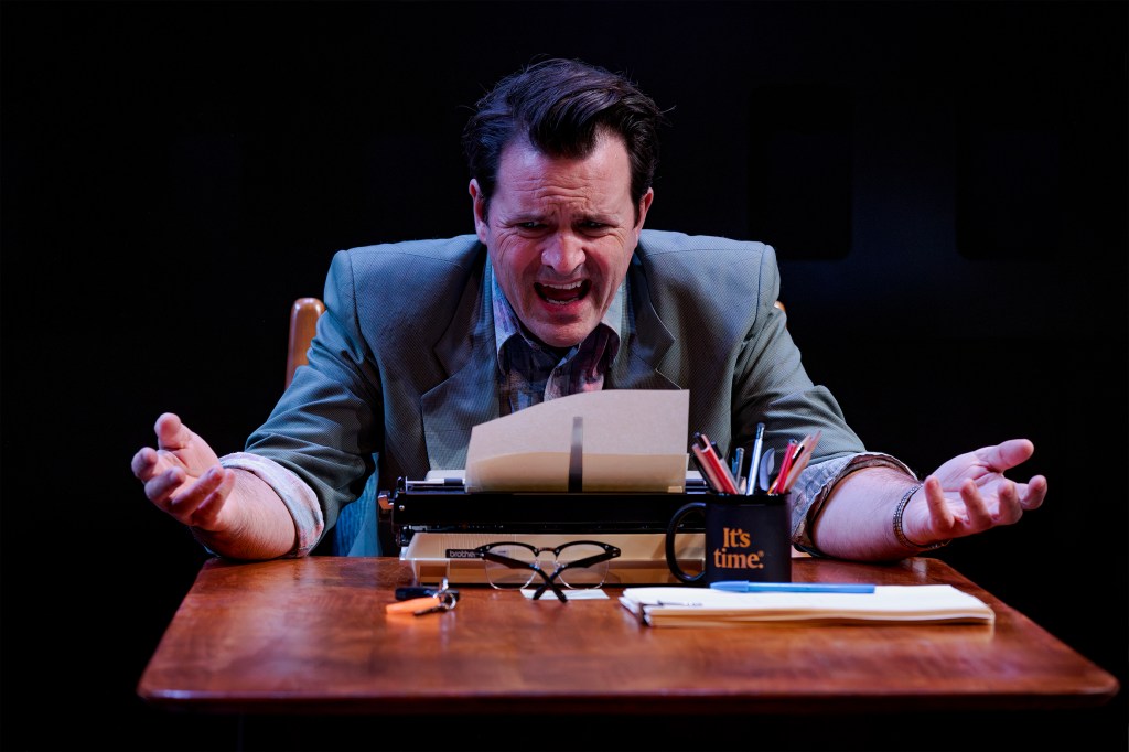 A solitary figure leans over a vintage typewriter on a desk, framed by moody stage lighting and props that evoke an era of artistic ambition