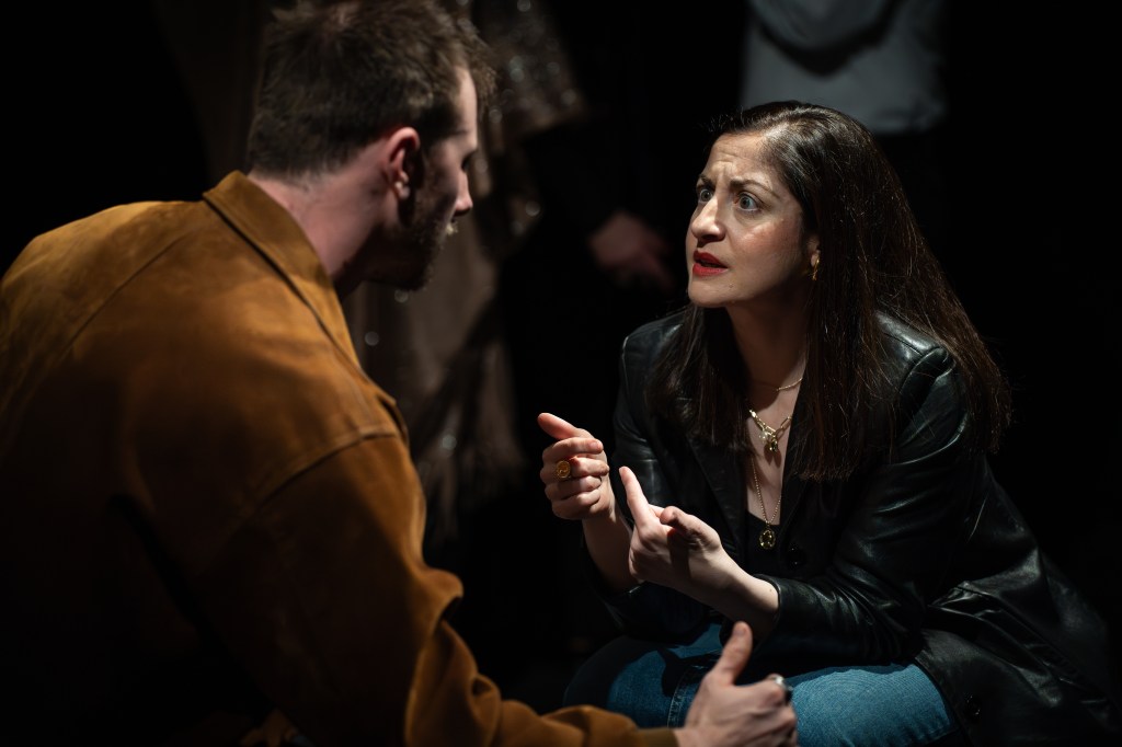 A dramatic scene featuring a man and a woman engaged in an intense conversation, with the woman gesturing expressively while the man listens attentively.